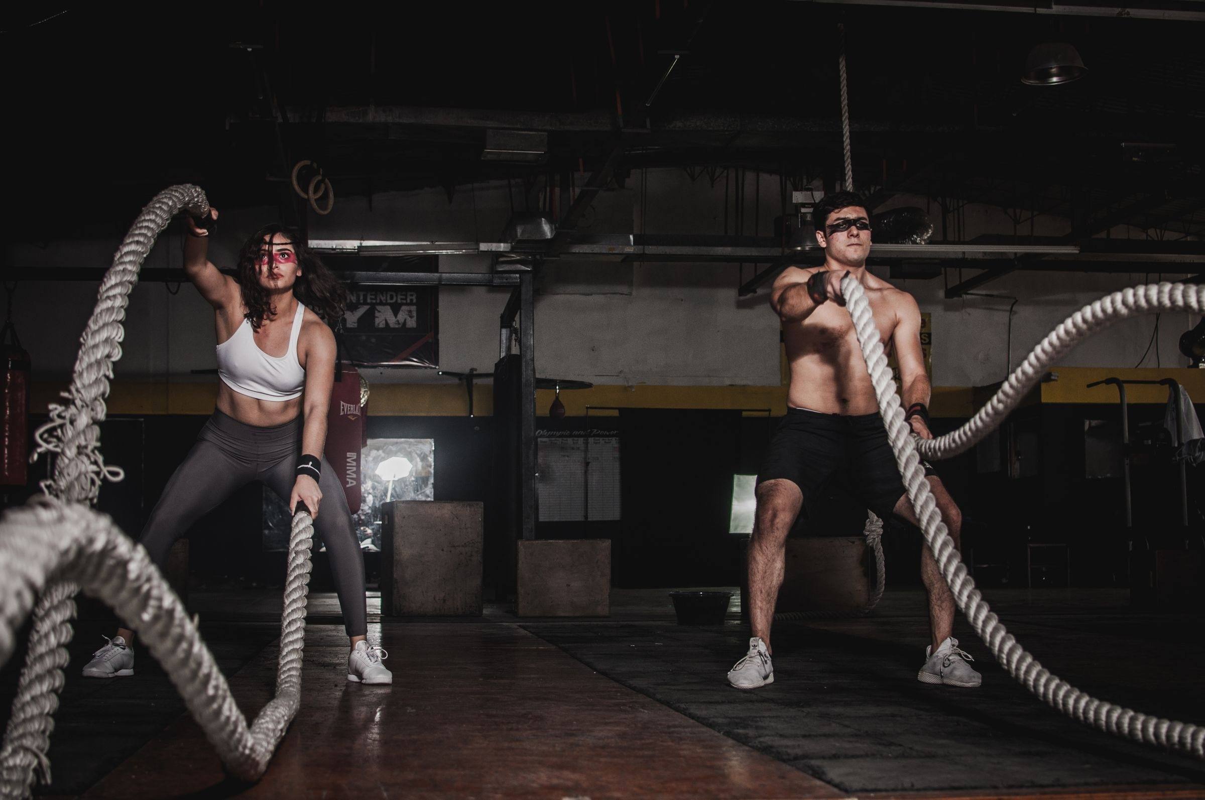 Two athletes slamming battle ropes in a dark training gym