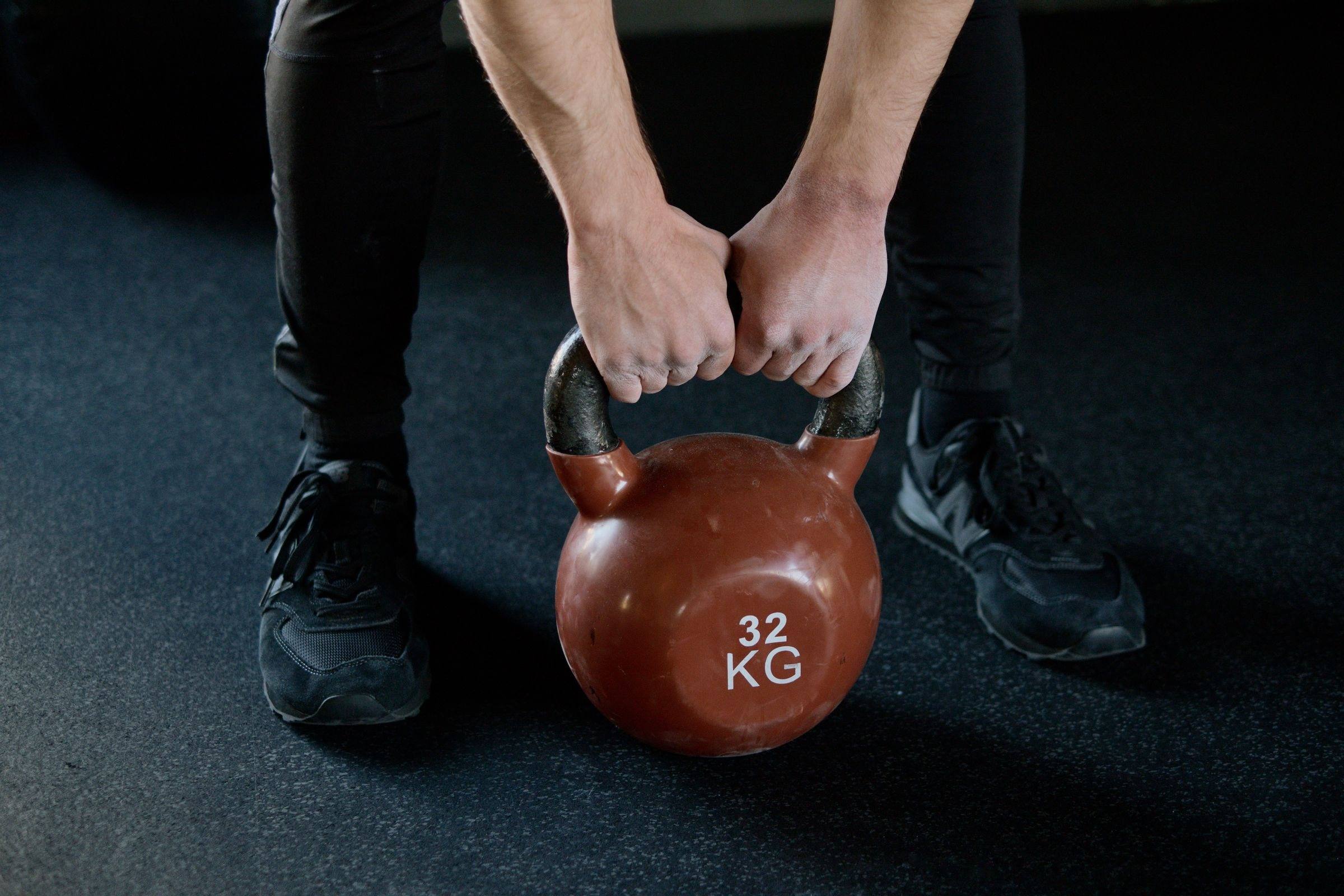 Close-up of hands gripping a 32 kg kettlebell on a gym floor