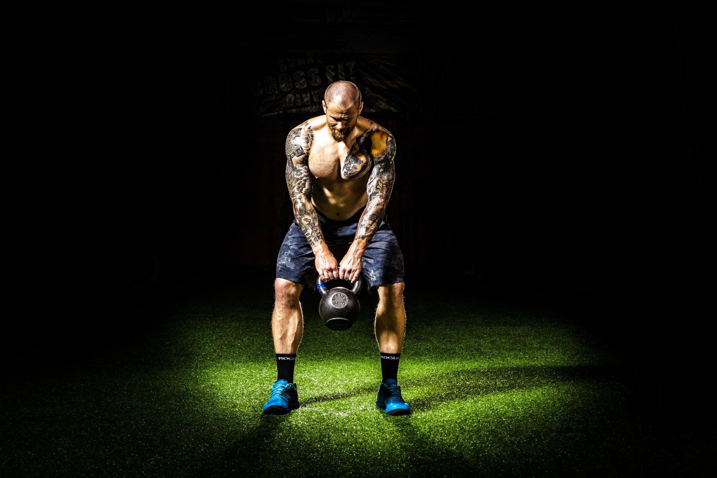 Tattooed athlete gripping a kettlebell under a single spotlight
