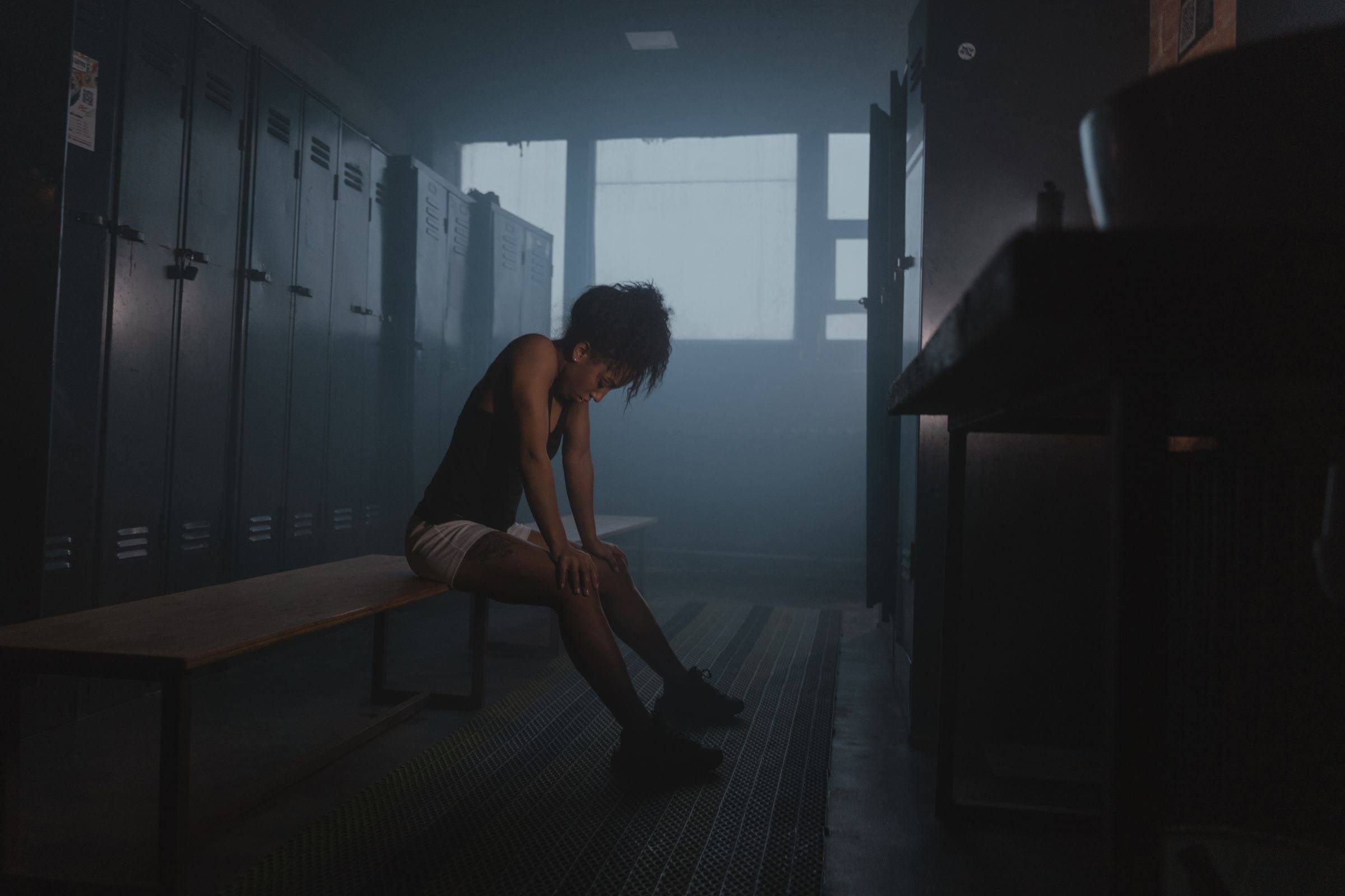 Athlete resting on a bench in a dim locker room