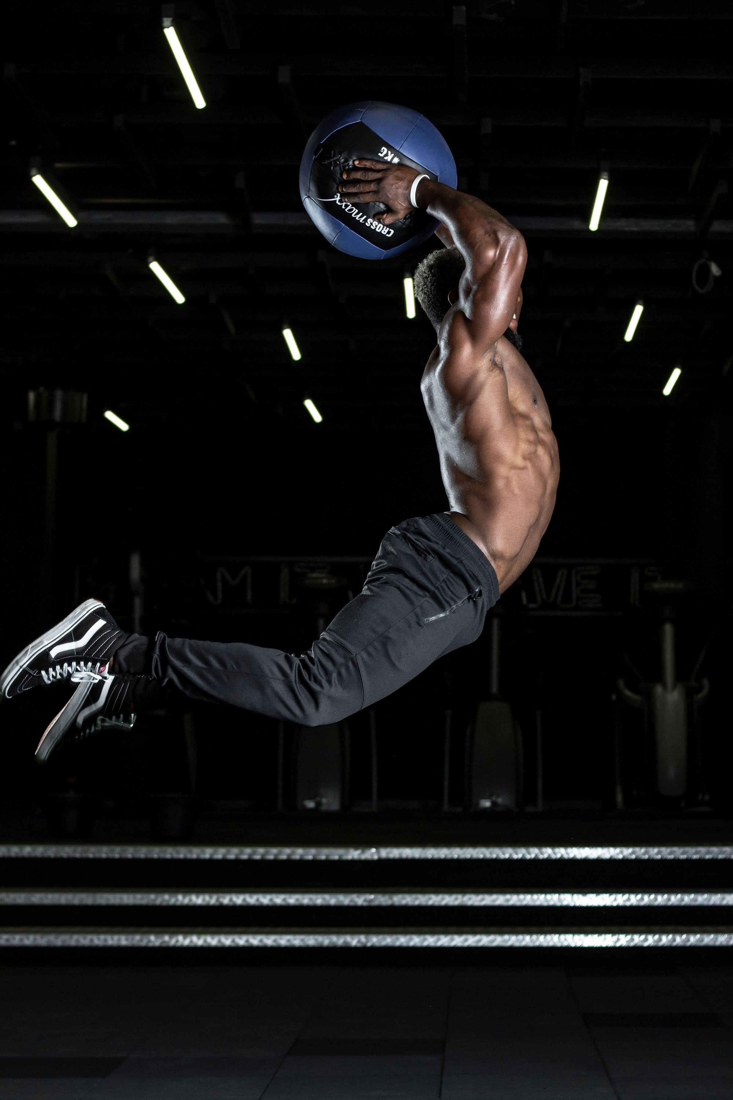 Athlete leaping with a medicine ball overhead against a black background
