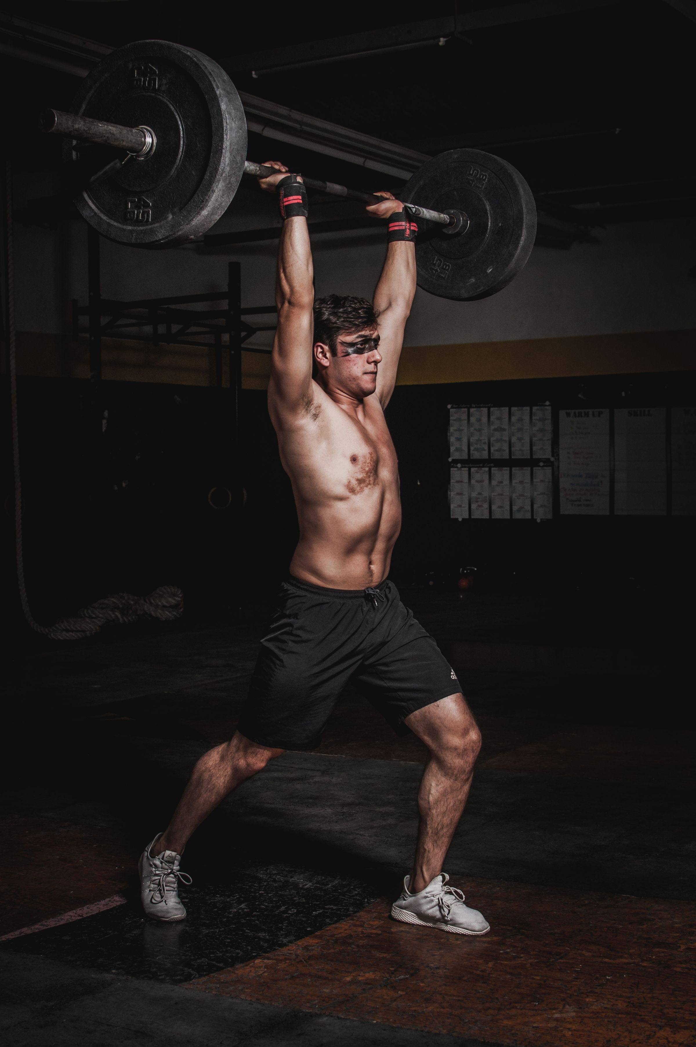 Athlete pressing a loaded barbell overhead in a dark gym