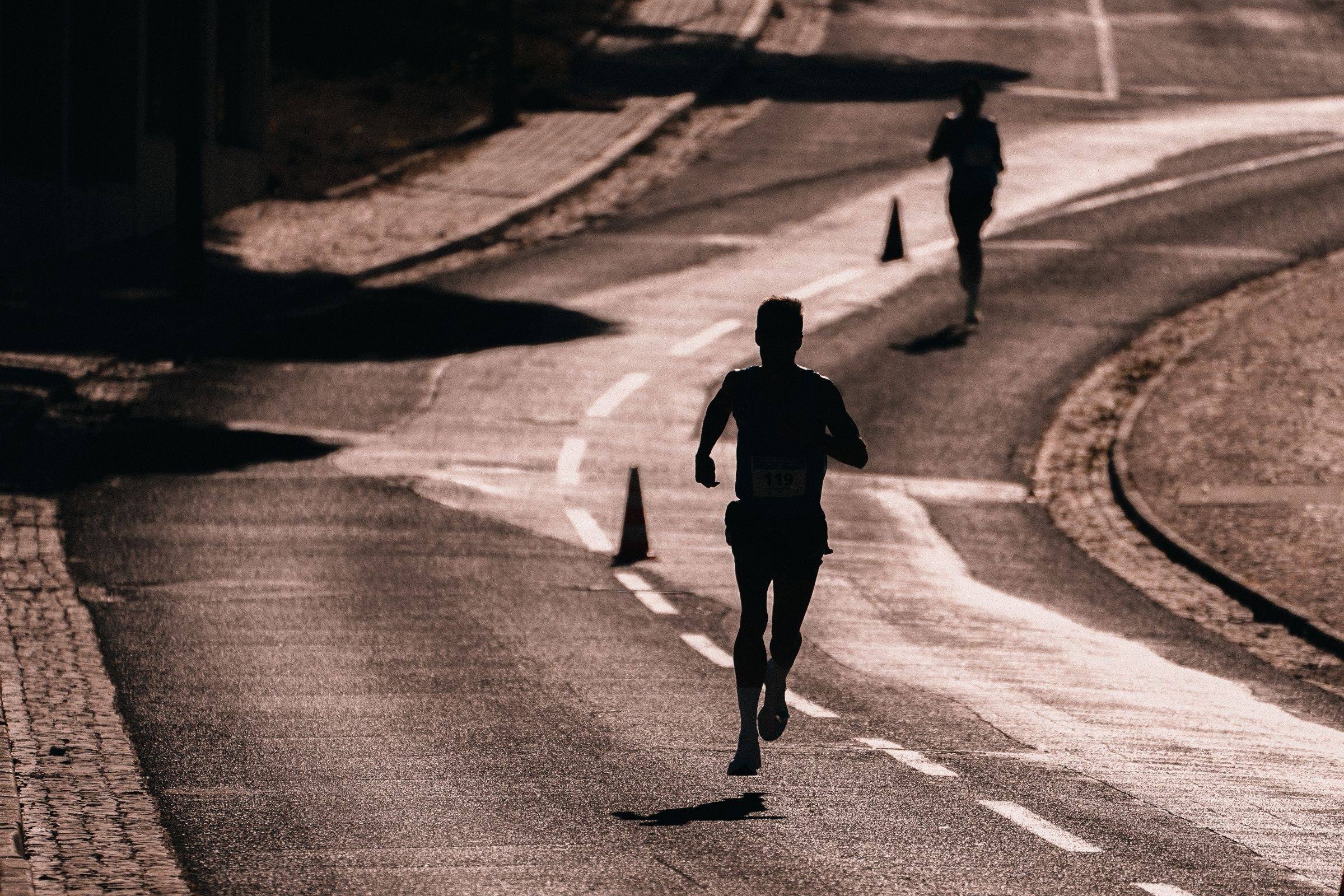Runner silhouetted on a winding road in low sun