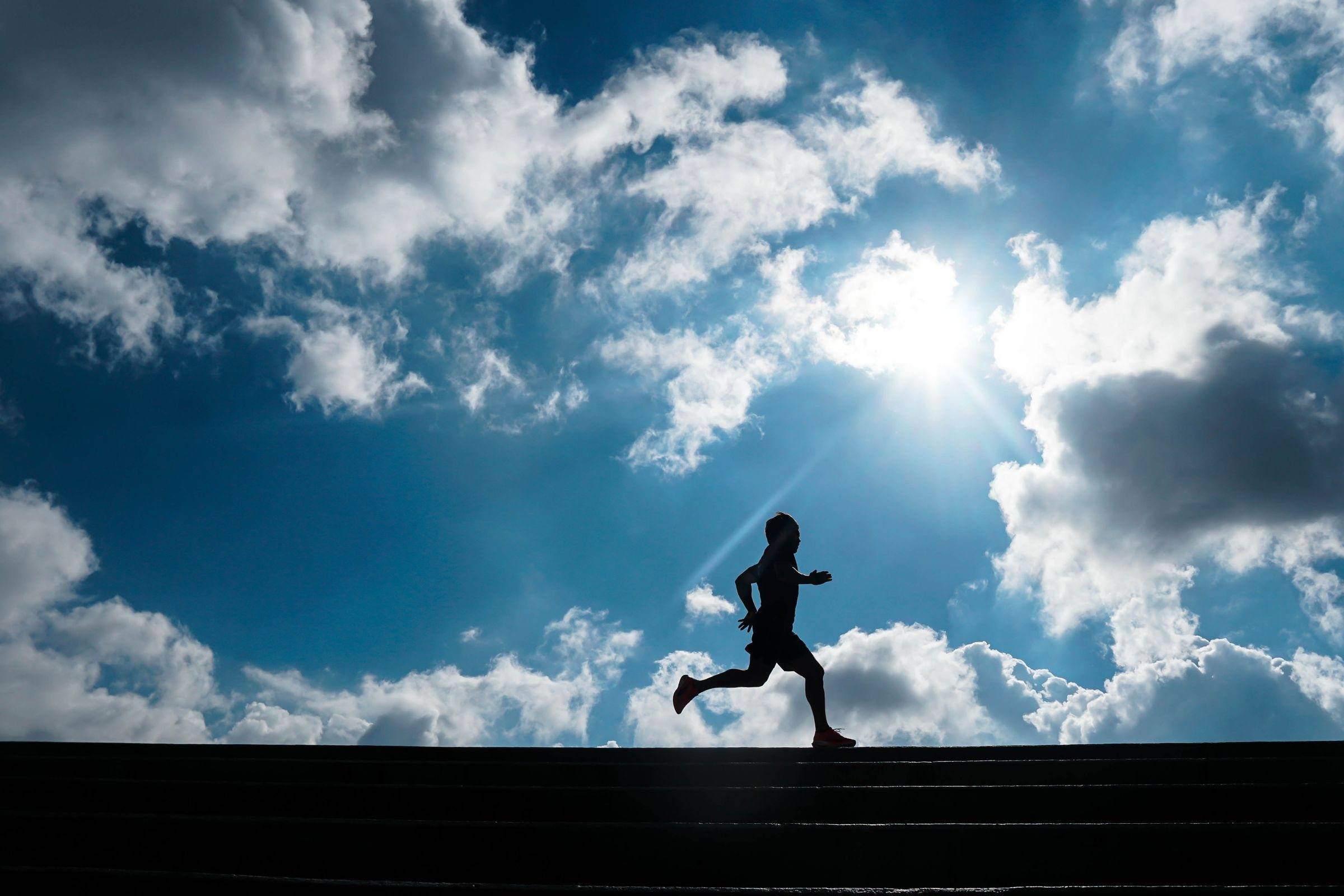 Runner silhouetted mid-stride against a bright sky and clouds